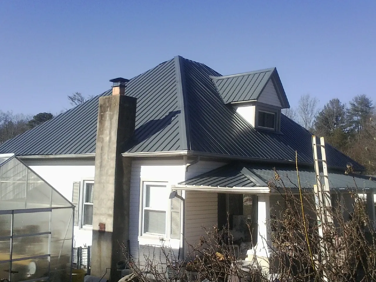 Dark blue standing seam metal roof on a white farmhouse with dormer — Slate & Tile Roof Repair by Roofing Brothers in Kohler