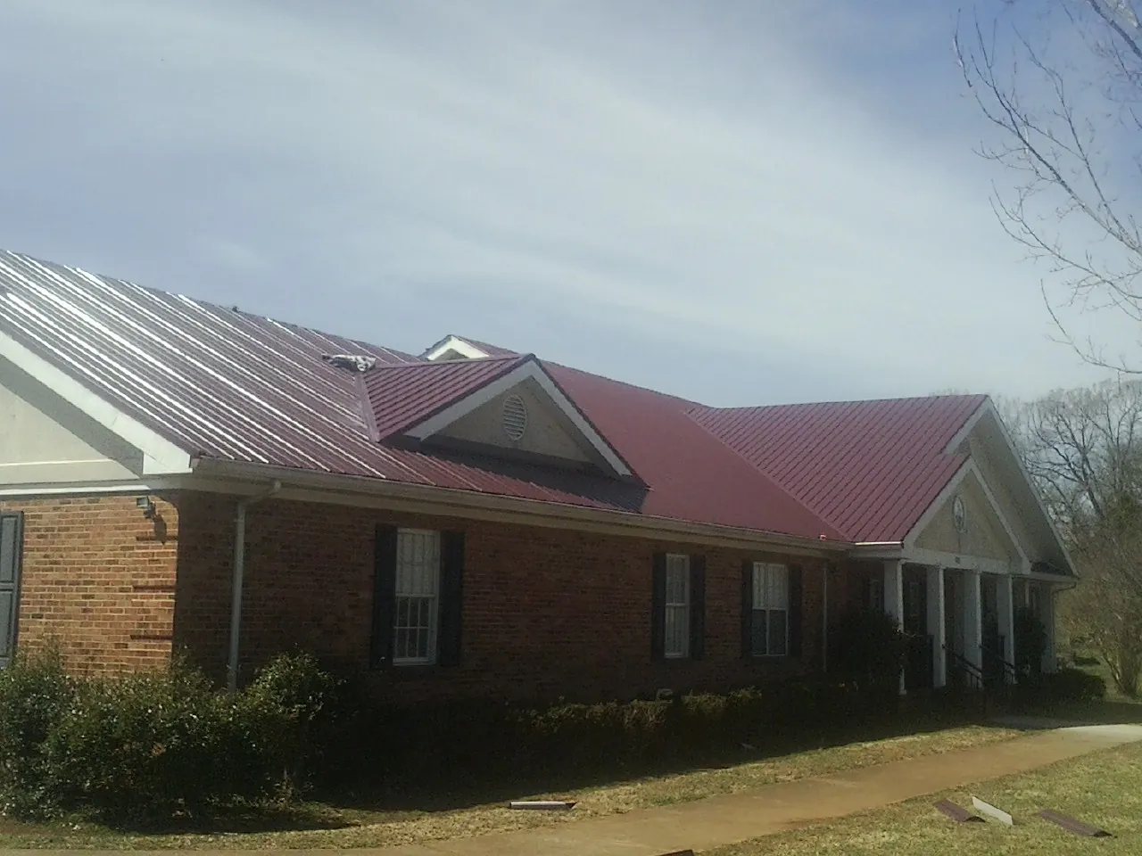 Red metal roof with gabled entries on a long brick building, from a Hail Damage Roof Repair job in Kohler