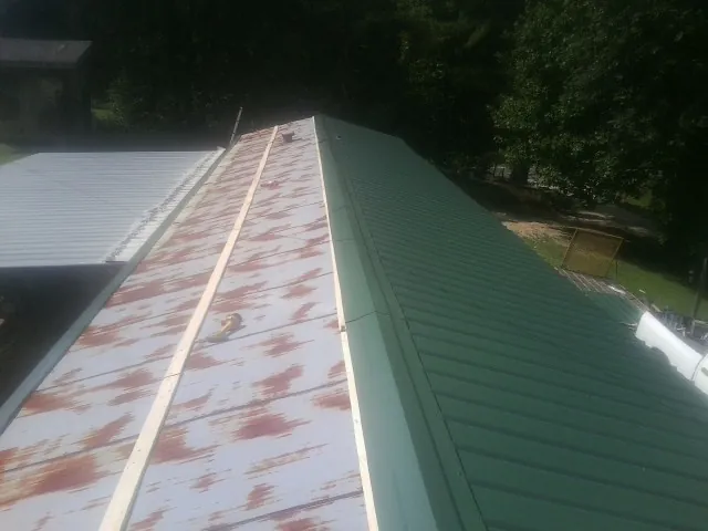 Old rusted panels beside newly installed green metal roofing — Wind Damage Roof Repair by Roofing Brothers in Kohler