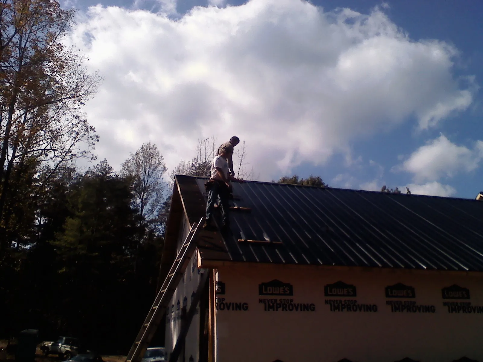 Roofer fastening dark metal panels high against a cloudy sky, from a Roof Inspection job in Kohler