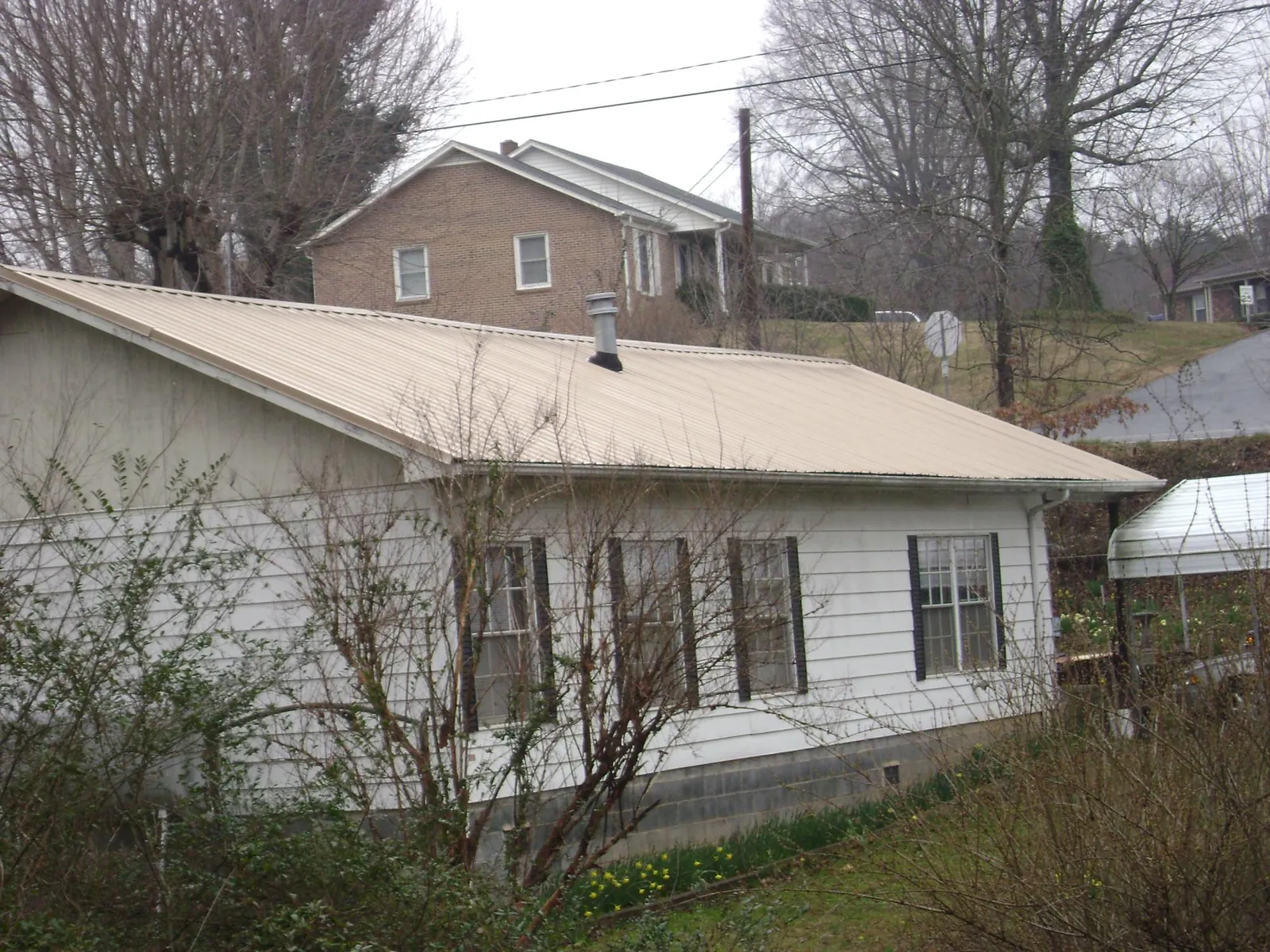 Tan metal roof on a white sided house set into a hillside — Commercial Roofing by Roofing Brothers in Kohler
